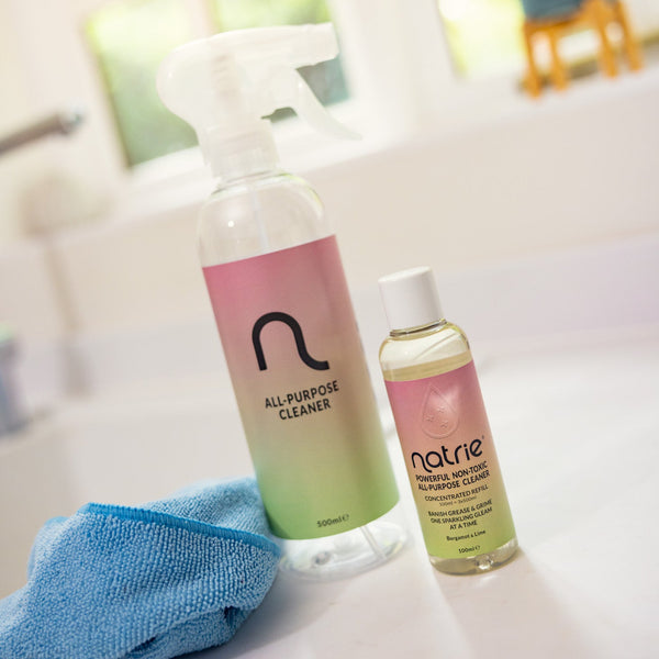 Two bottles of Natrie cleaning products on a white surface with a blue cloth.