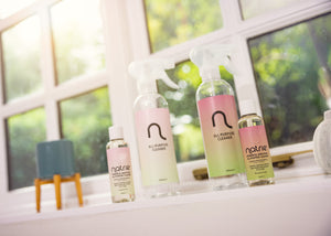 Set of Natrie cleaning products on a windowsill with a blurred green outdoor background