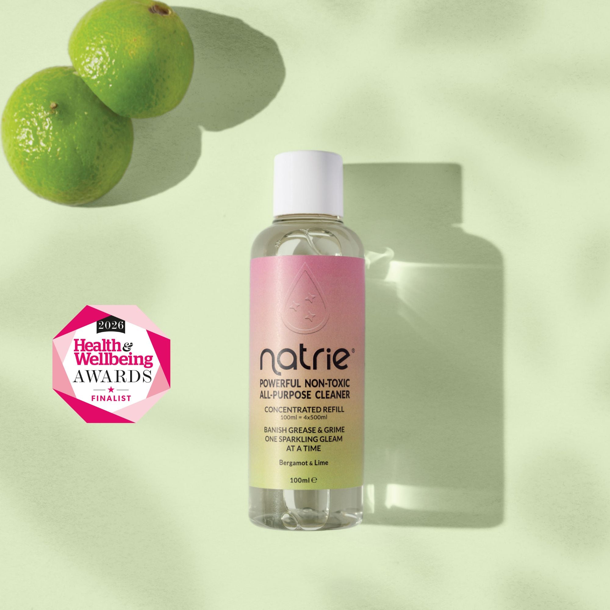 A bottle of Natrie Powerful Non-Toxic All-In-One Cleaner with a pink label and white cap, set against a light green background with lime graphics and a pink Health & Wellness Awards 2025 badge.